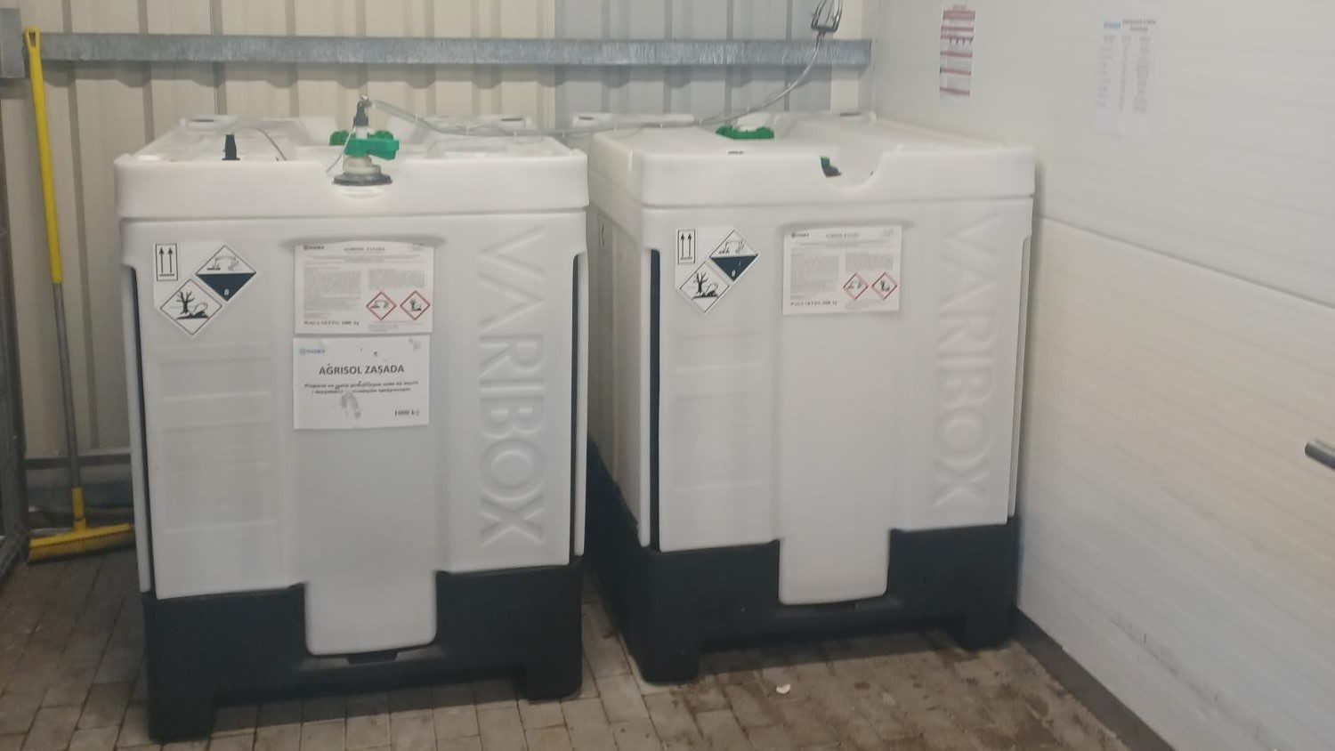 Dwa pojemniki IBC VARIBOX z etykietami ostrzegawczymi w magazynie